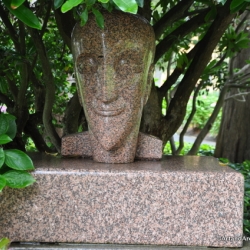 a smiling marble face statue underneath a tree